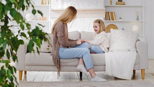 Young Mother Woman Babysitter with Little Girl Daughter Sitting in Living Room Sofa Talking Chatting