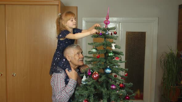 Little Child Girl with Senior Grandparent Decorating Artificial Christmas Tree at Oldfashion Home