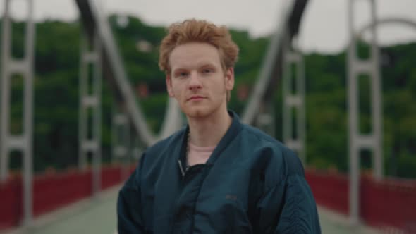 Portrait of Redhead Young Man in Stylish Wear Holding Smartphone in Hands Looking at Camera Standing