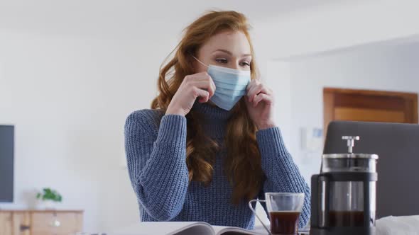 Woman wearing face mask drinking coffee at home