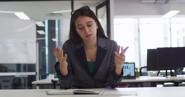 Caucasian businesswoman sitting at desk having video call gesturing