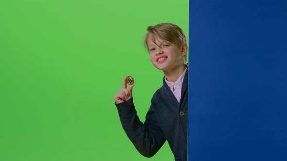 Teenager Peeks Out From Behind a Board Shows the Coin and the Trumb Up on a Green Screen