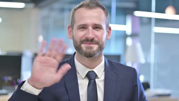 Portrait of Young Businessman Waving at Camera in Office