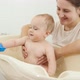 Smiling Mother Holding and Looking at Her Baby Son Playing in Small Children Bath at Home - VideoHive Item for Sale