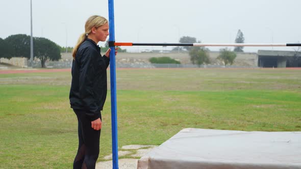 Side view of Caucasian female athlete checking high jump bar at sports venue 4k