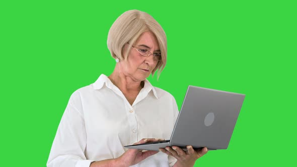 Serious Mature Business Woman in Glasses Using Laptop on a Green Screen, Chroma Key.