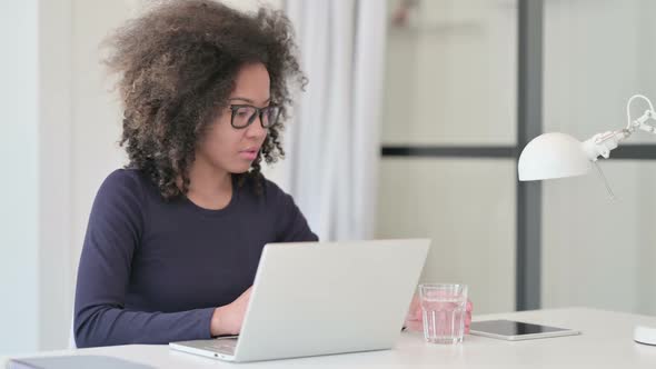 African Woman Drinking Water While Using Laptop