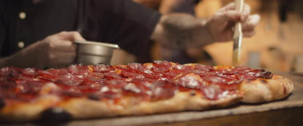 Italian chef spreading olive oil with brush over traditional pepperoni al taglio pizza. Close up