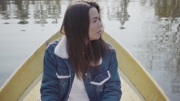 Portrait of a Charming Young Woman Wearing a Denim Jacket Floating on a Boat on a Lake or River
