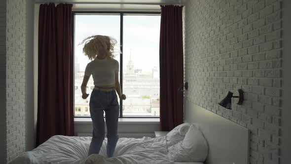 Happy Woman with Cute Curls Cheerfully Jumping on the Bed in the Bedroom
