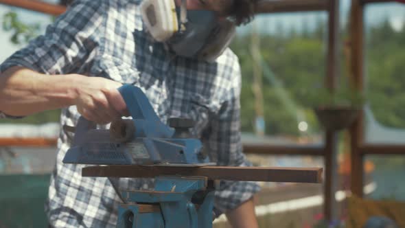 Young caucasian man planing teak wood timber with electrical planer