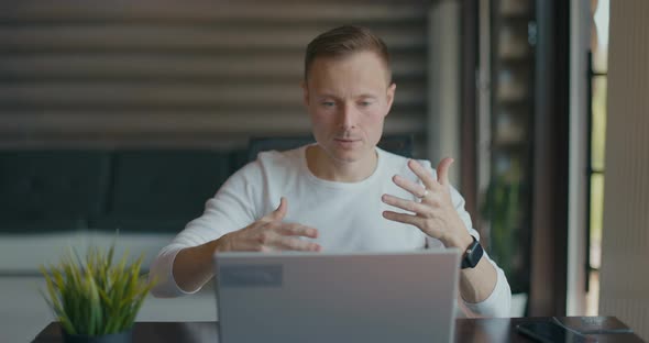 Concentrated Young Man Makes Video Call on Laptop While Sitting in Room at His Desk