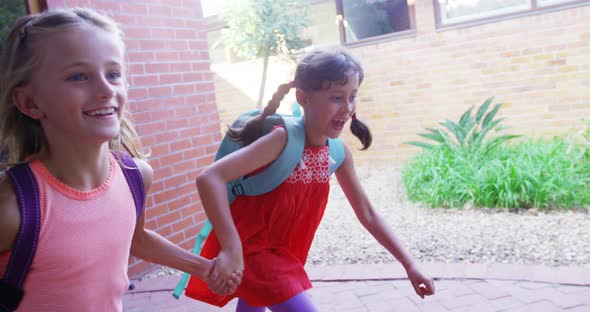 School girl holding hands and running together in corridor at school