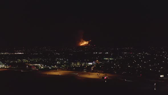 Human caused wildfire breaks out in the foothills above a sprawling suburb and highway at night - ae