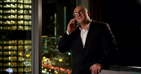 Bald Businessman in Glasses and a Suit Is Talking on a Smartphone, Smiling