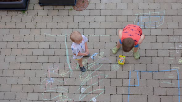 Two young boys drawing on paving slabs with colorful chalks.