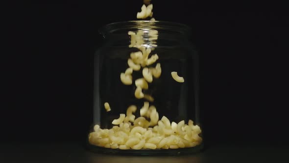 Uncooked Macaroni Falls Into Empty Glass Jar On Black Background