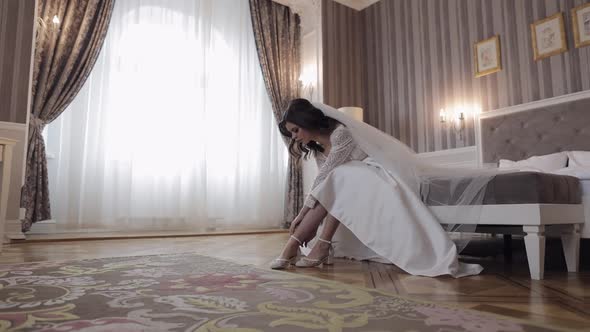 Young Bride in White Wedding Dress Wearing High Heeled Shoes on Slim Legs While Sitting at Home