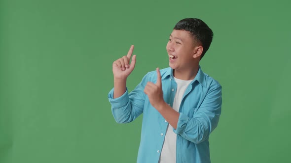 The Inspired Young Asian Boy Smile And Pointing To The Side While Standing In The Green Screen