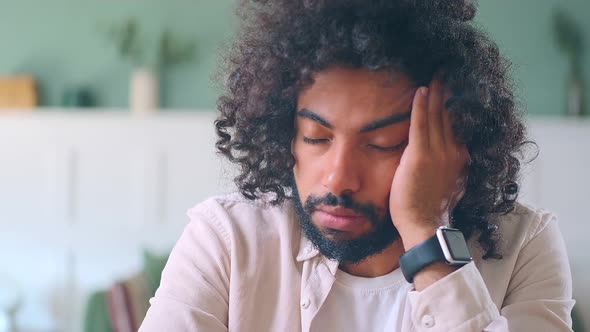 Young Tired Brunet Arabian Man Touches Face Sits at Table in Own Living Room