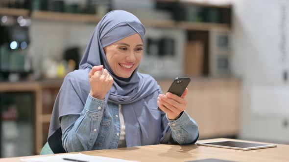 Young Arab Woman Celebrating Success on Smartphone in Cafe 