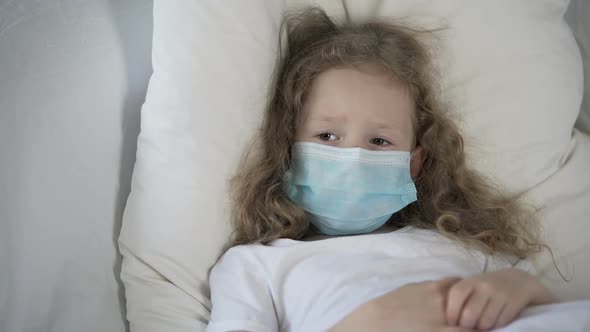 Sad Child in Medical Face Mask Lying in Bed, Suffering Rare Disease, Epidemic
