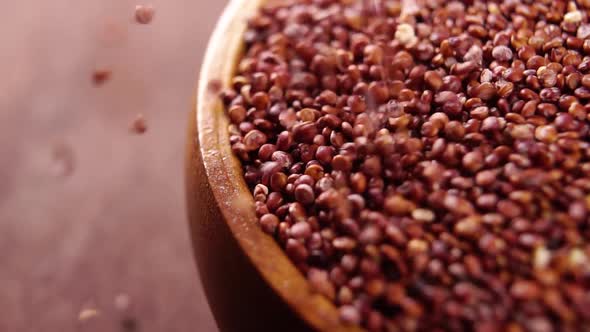Red quinoa in rustic bowl on wooden kitchen board. Falling raw grain in slow motion. Macro