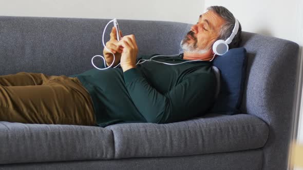 Man listening to music on mobile phone while lying on sofa 4k