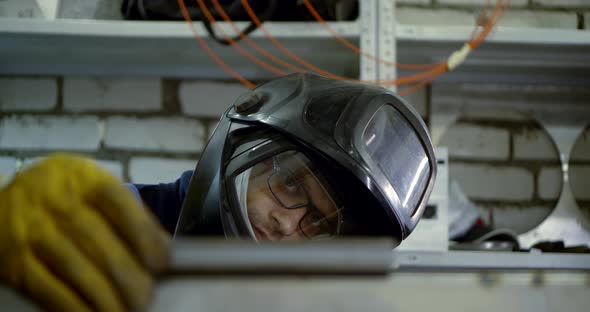 Close-up Portrait of a Welding Master-a Man in Gloves and a Helmet Working with a Detail That Cooks