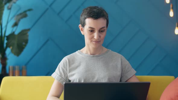 Short-haired woman looks laptop, looking the camera, spreading her arms out in frustration.