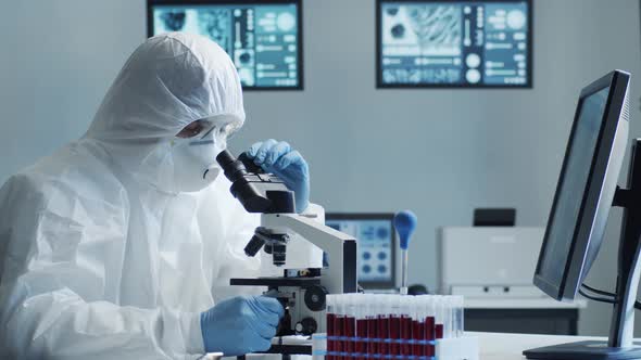 Scientist in protection suit and masks working in research lab using laboratory equipment.