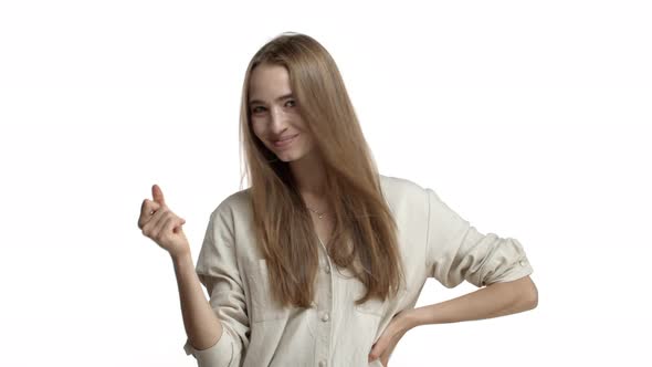 Studio Shot of Attractive Blond Woman with Long Hair Wearing Beige Blouse Snapping Fingers to Create