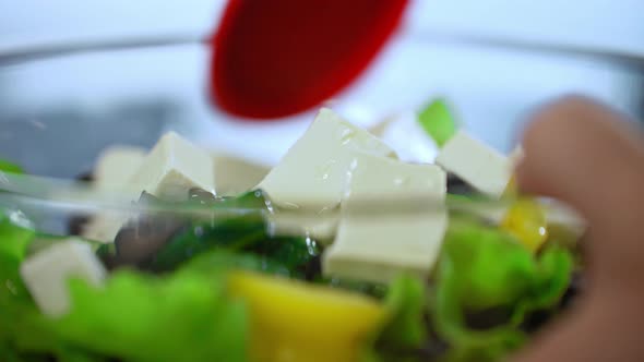 Olive oil is poured into the salad. A man stirs fresh salad in a large glass plate on the table.