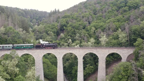 Steam engine train driving on a stone viaduct over a valley,zoom.