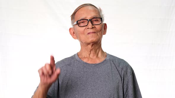Excited and smiling elderly man pointing up on empty space on white studio background.