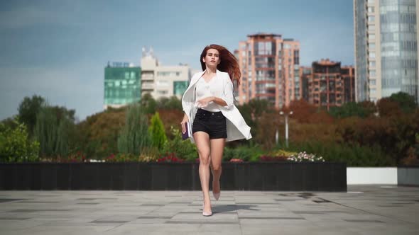 Beautiful business woman with a phone and a notebook in her hands is late and runs in heels to work