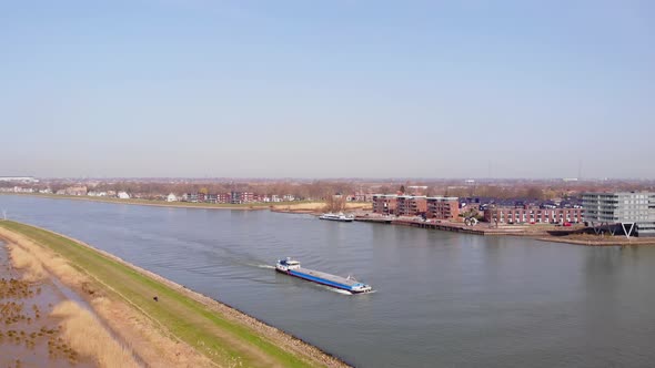 Aerial Flying Over Grass Verge Beside Crezeepolder Nature Reserve With Ship Passing On River Noord O