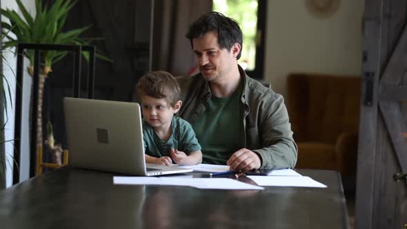 Father is trying to work and play with a little boy at same time at home.