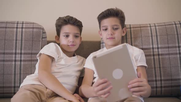 Front View Close-up of Two Caucasian Twin Brothers Looking at Tablet Screen and Smiling
