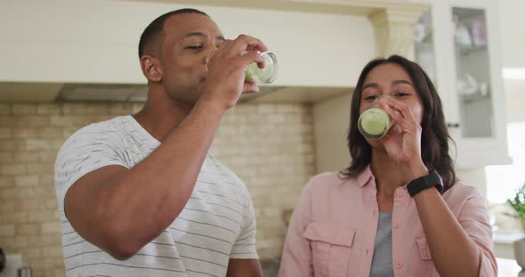 Happy biracial couple drinking self-made smoothie in kitchen