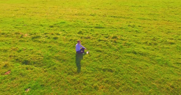 Low Orbital Flight Around Man on Green Grass with Notebook Pad at Yellow Rural Field