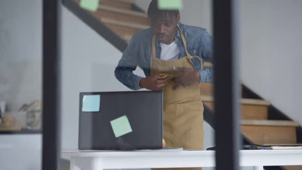 Young Man in Apron Hurrying to Laptop on Table and Typing on Keyboard