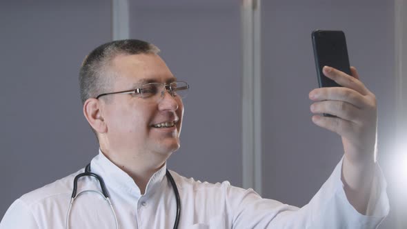 male doctor smiles and grimaces while taking a selfie on his phone