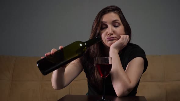 Woman Pours Wine Into Glass Sitting Stressed and Depressed