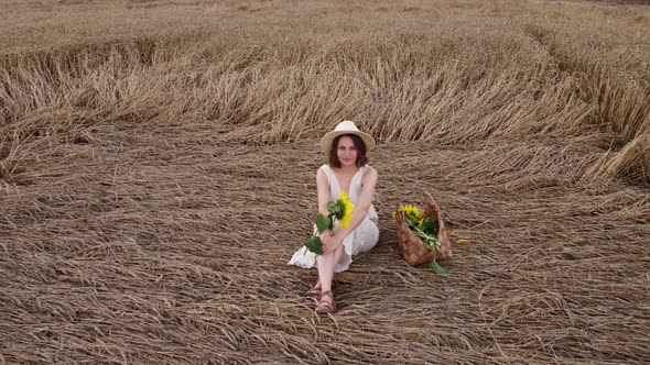 beautiful smiling young woman in dress is sitting on a wheat field. summer holiday concept.