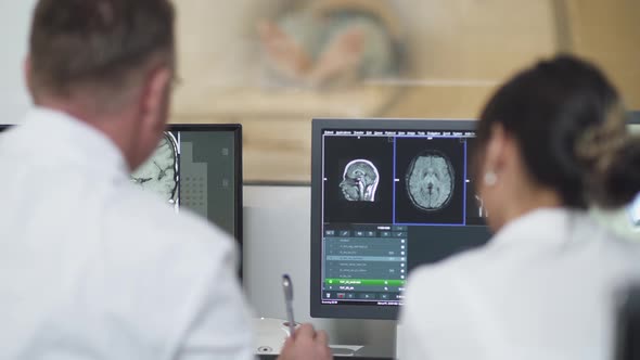 Magnetic Resonance Imaging, Adult Man and Asian Woman Professional Doctors Examines the Results of