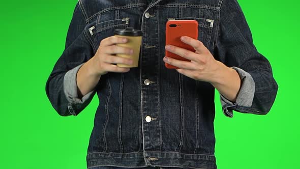 Guy Holding Red Phone in His Hands and Drinking Coffee While Walking, Close Up. Green Screen. Slow