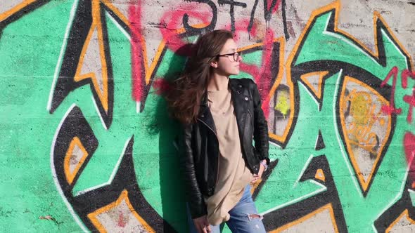 Teenage Girl in Casual Outfit Posing in Front of Graffiti Wall on Windy Sunny Day