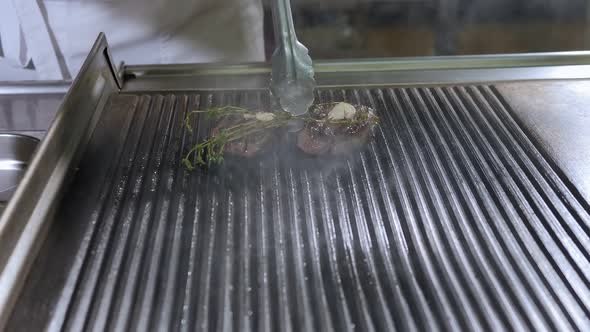 Closeup of the Chef Frying a Juicy Steak on the Grill in the Restaurant Kitchen