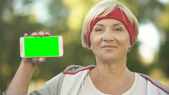 Smiling Fit Middle-Aged Woman Showing Green Screen Mobile Phone Sports App